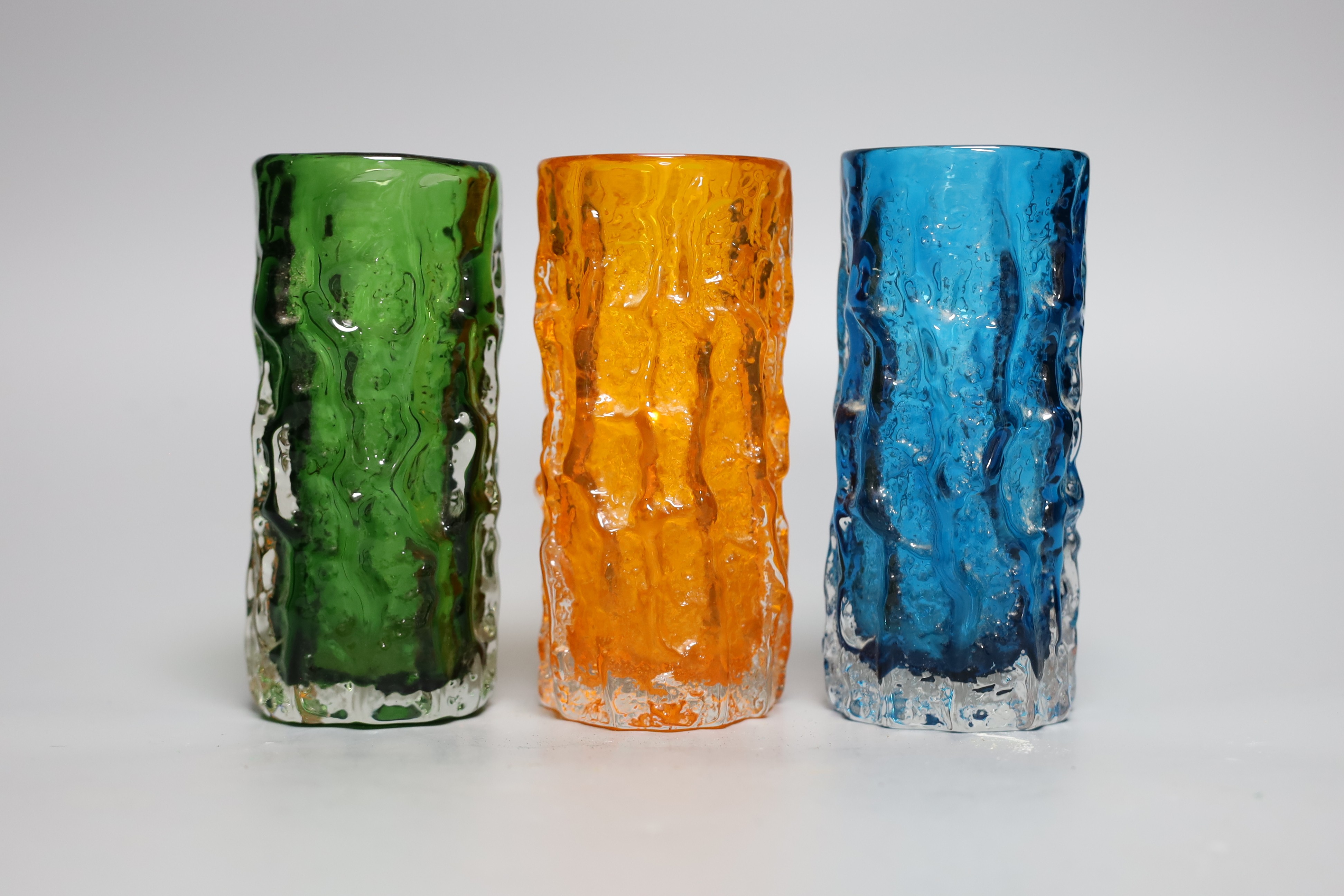 Three Whitefriars 'bark' cylinder vases, model 9689 designed by Geoffrey Baxter, kingfisher blue, tangerine and green glass, each 15cm high.